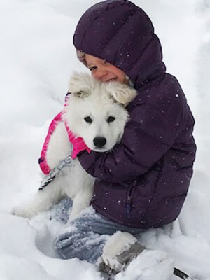 little girl hugging white swiss shepherd puppy in the snow